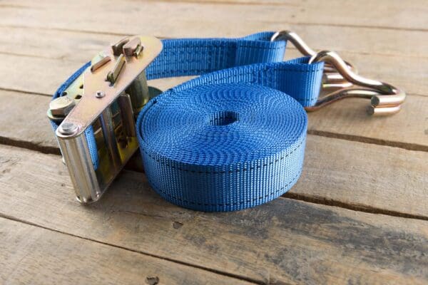 Blue ratchet strap coiled on wooden surface with metal ratchet.